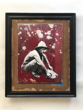 Load image into Gallery viewer, mixed media black and white crouching man holding a large shell red arty  background  with white paint spots in vintage black frame
